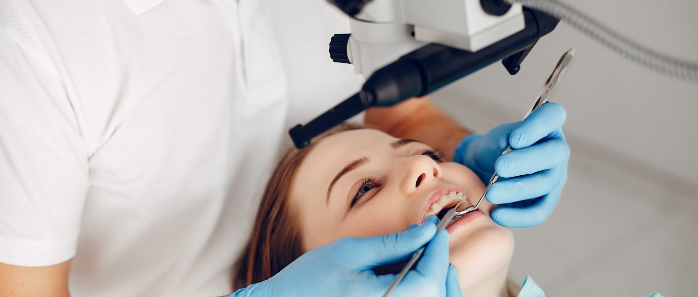 Lekarz dentysta Czyżyny wykonuje precyzyjny zabieg leczenia pod mikroskopem u pacjentki noszącej aparat ortodontyczny.