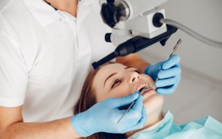 Lekarz dentysta Czyżyny wykonuje precyzyjny zabieg leczenia pod mikroskopem u pacjentki noszącej aparat ortodontyczny.