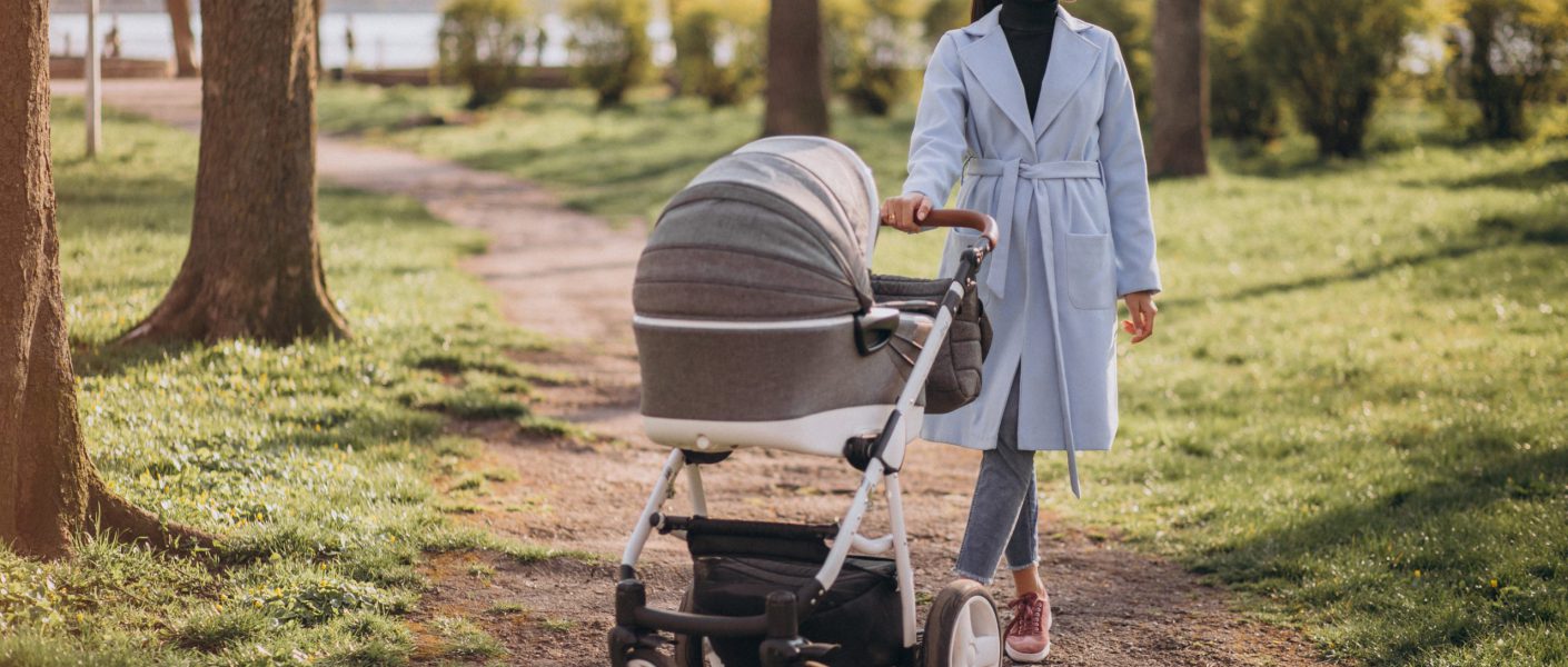 Młoda mama spaceruje po parku, prowadząc elegancki wózek z gondolą – polskie wózki dziecięce na codzienne spacery