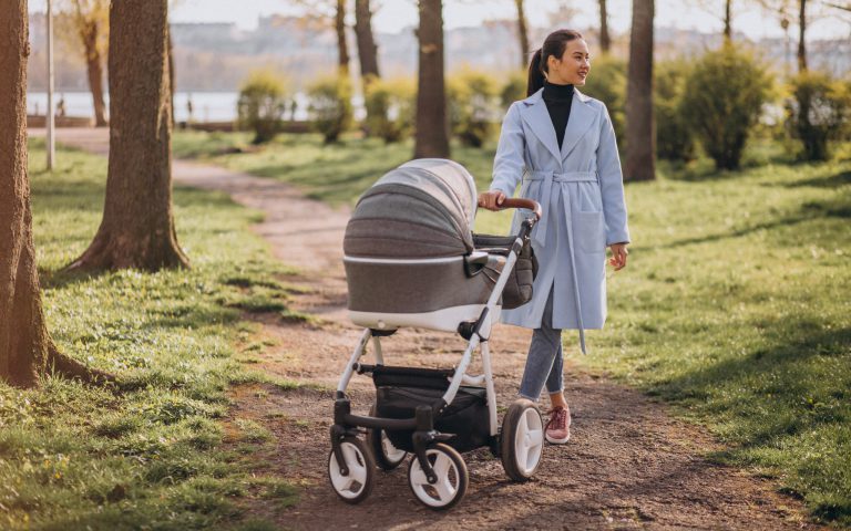 Młoda mama spaceruje po parku, prowadząc elegancki wózek z gondolą – polskie wózki dziecięce na codzienne spacery
