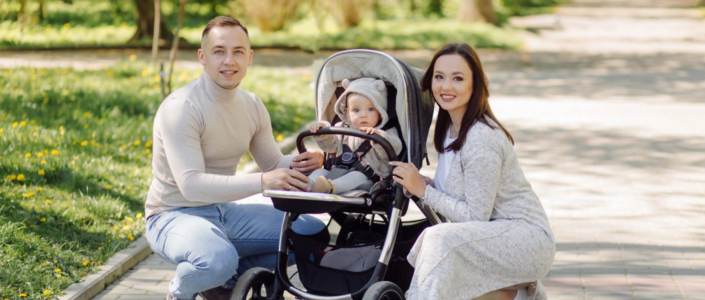 Szczęśliwa rodzina na spacerze w parku, rodzice pozują z niemowlęciem siedzącym w nowoczesnym wózku dla dzieci