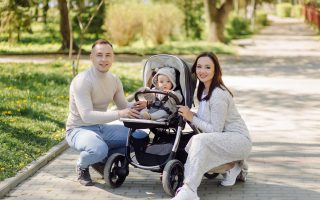 Szczęśliwa rodzina na spacerze w parku, rodzice pozują z niemowlęciem siedzącym w nowoczesnym wózku dla dzieci