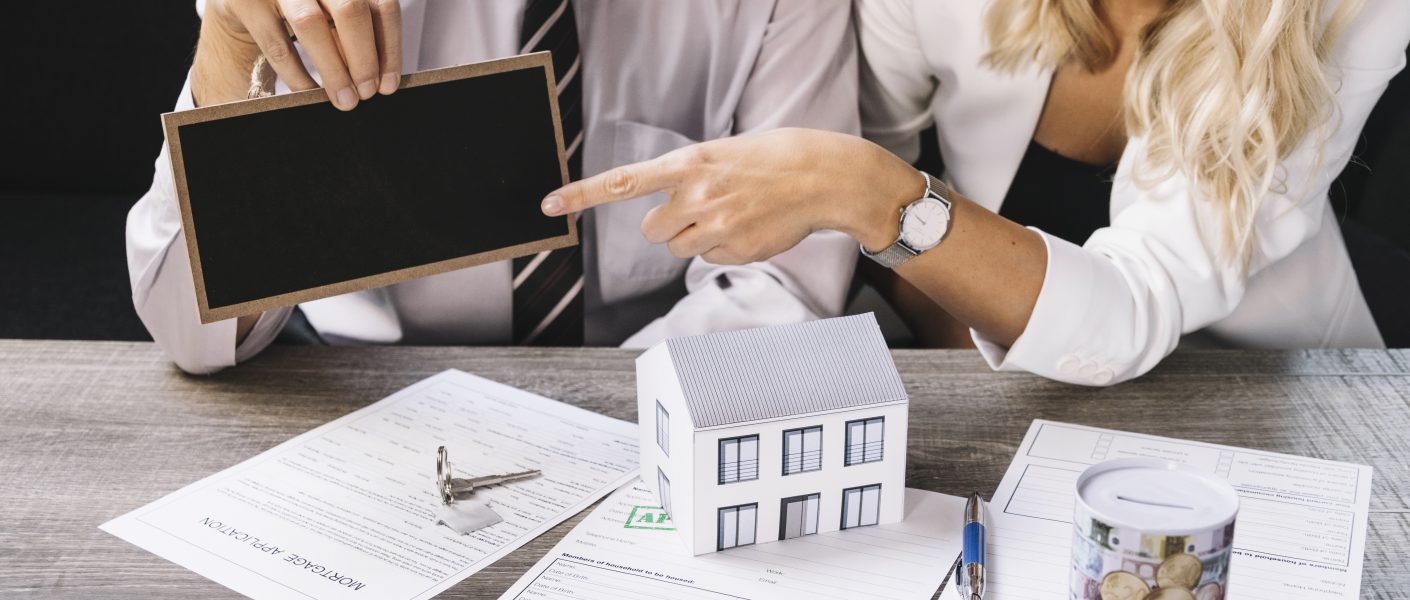 Profesjonalne spotkanie przy biurku z dokumentami, kluczami i modelem domu, podczas którego omawiane są szczegóły umowy, jaką oferuje skup nieruchomości z lokatorami na dany lokal.