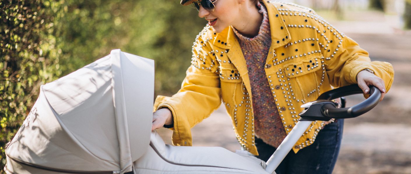 Młoda mama sprawdza beżowe wózki Warszawa sklep stacjonarny na ścieżce w otoczeniu zieleni.