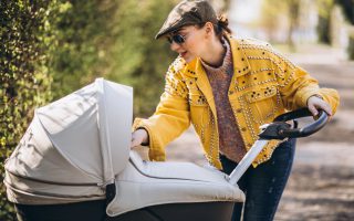 Młoda mama sprawdza beżowe wózki Warszawa sklep stacjonarny na ścieżce w otoczeniu zieleni.