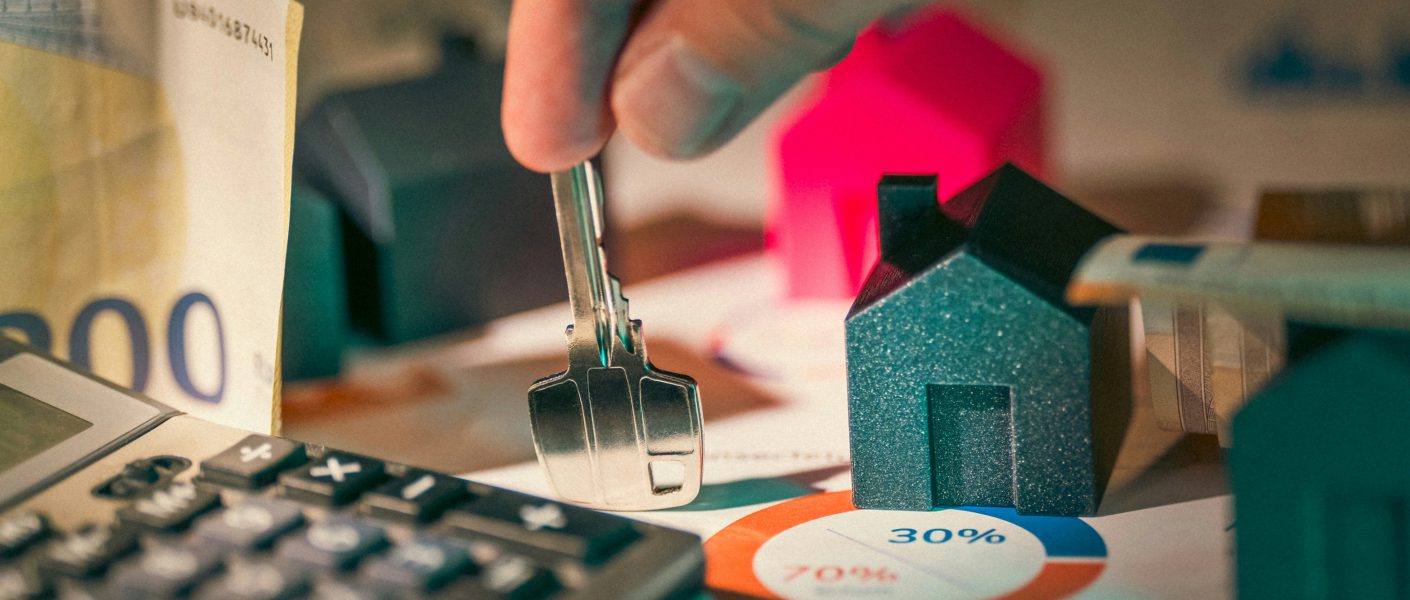 Na zdjęciu przedstawiono rękę trzymającą klucz nad dokumentami finansowymi