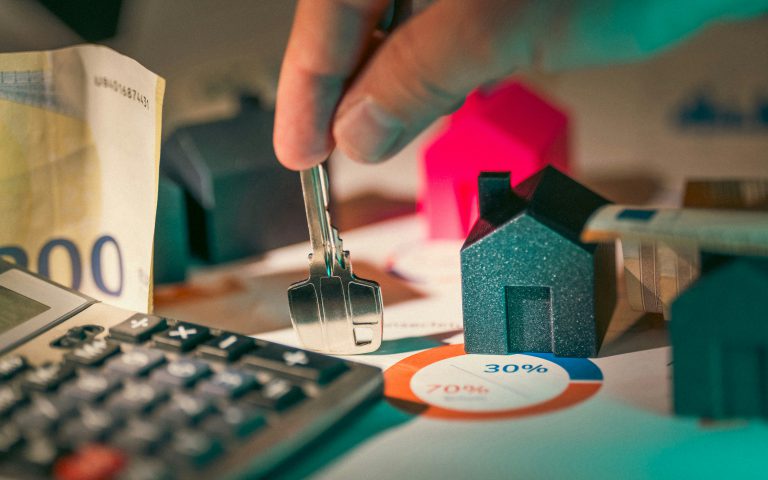 Na zdjęciu przedstawiono rękę trzymającą klucz nad dokumentami finansowymi