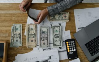 Doradca finansowy Wrocław analizujący wykresy i dokumenty finansowe, przeliczający gotówkę przy użyciu kalkulatora w telefonie i laptopa.