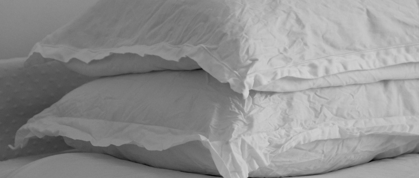 Na zdjęciu widać dwie białe poduszki ułożone jedna na drugiej na łóżku