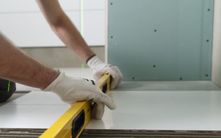 mężczyzna układa płytki przy pomocy poziomica - remont kuchni gdynia