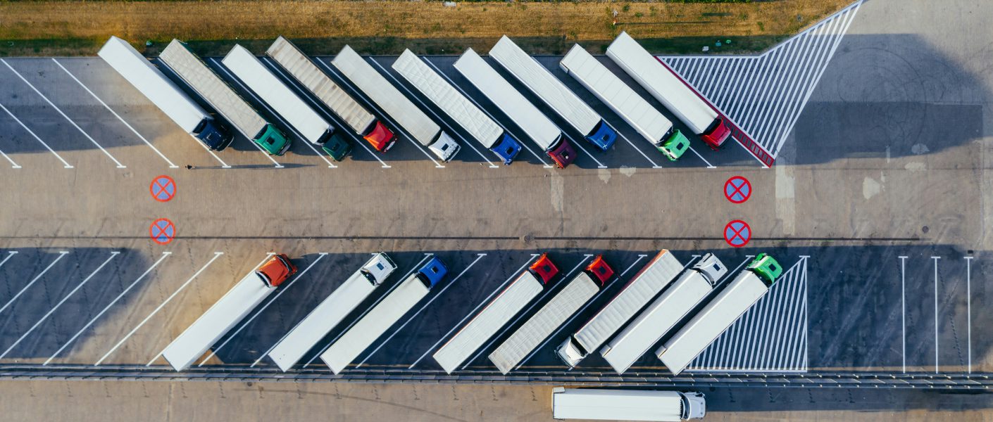 Na zdjęciu widok z lotu ptaka przedstawia parking dla samochodów ciężarowych z ustawionymi równolegle naczepami.