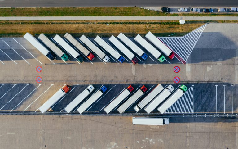 Na zdjęciu widok z lotu ptaka przedstawia parking dla samochodów ciężarowych z ustawionymi równolegle naczepami.